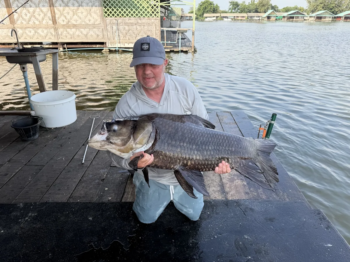 An angler holding a dark scaled fish low over a wet mat