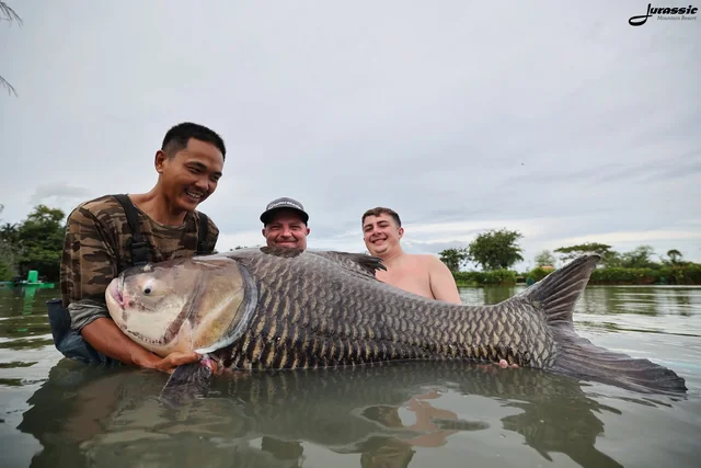 Vinny and Finlay in the water beside a guide supporting a large carp.
