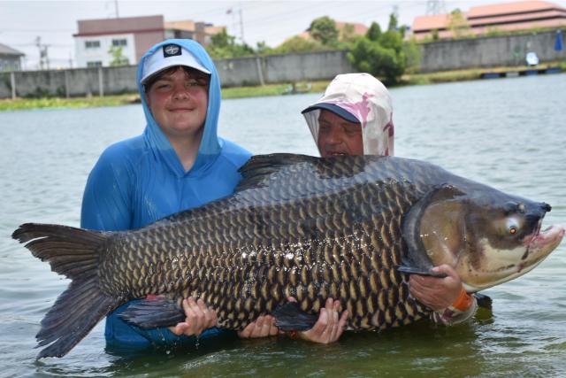 Two anglers supporting a large scaled fish in the lake