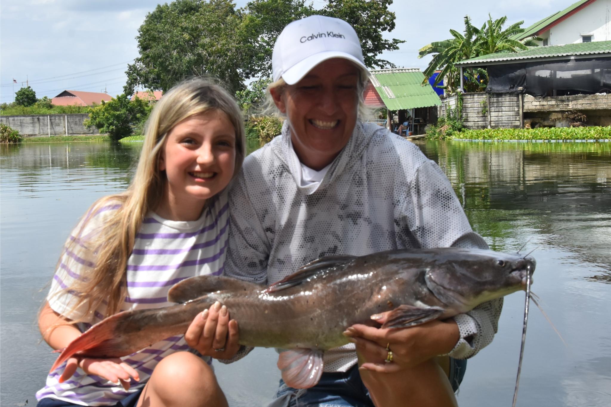 Two family members posing with a catfish beside the lake