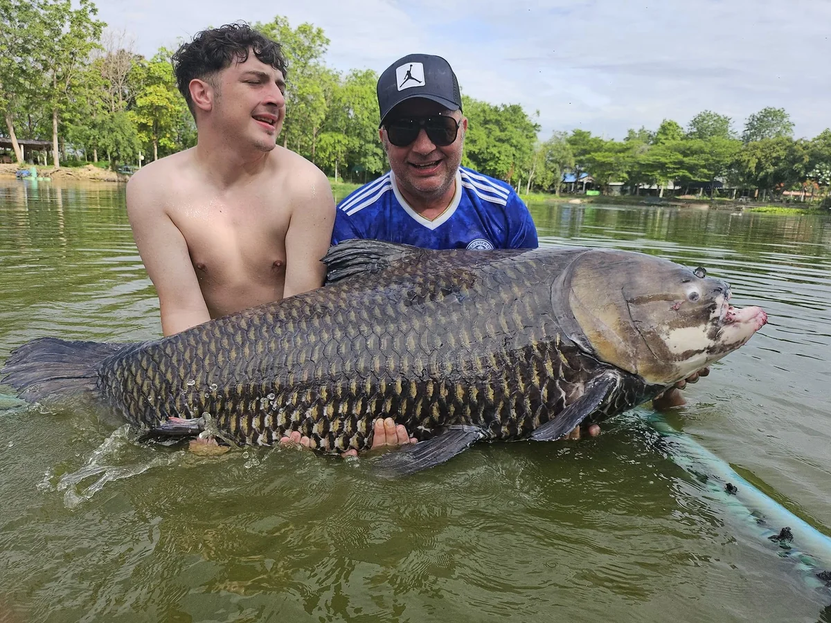 Finlay and Vinny, wearing a blue football shirt, supporting a carp together in the water.