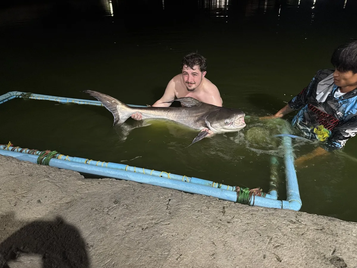 An angler and another person with a long fish above a blue-framed net at night
