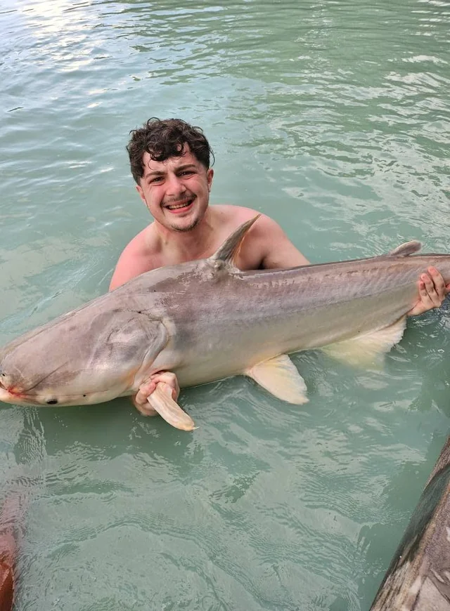 Finlay smiling with a catfish supported at the water’s surface.