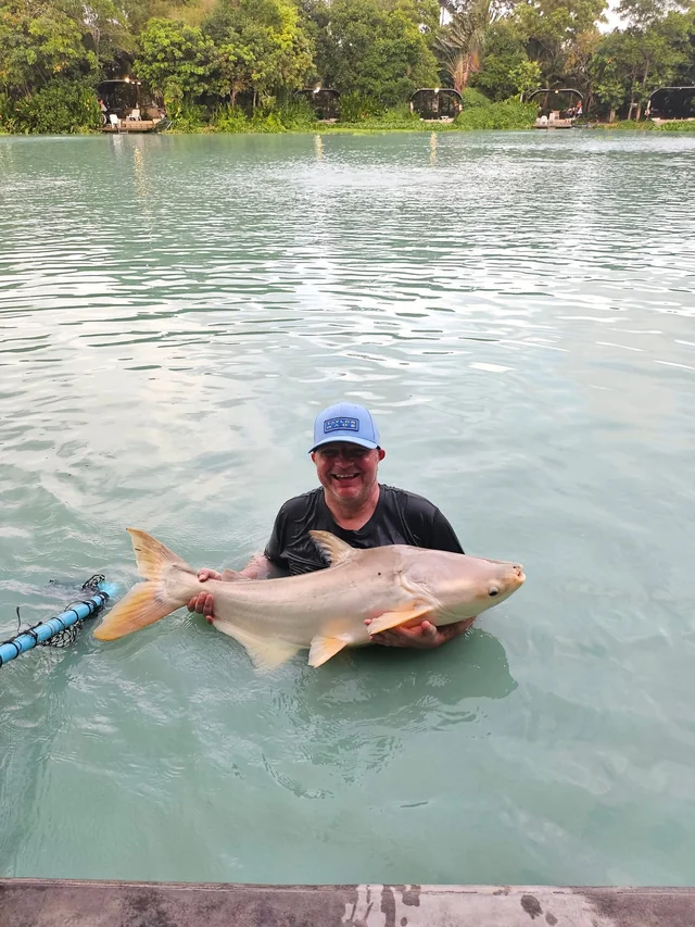 Vinny supporting a pale catfish in the water, with the lake behind him.