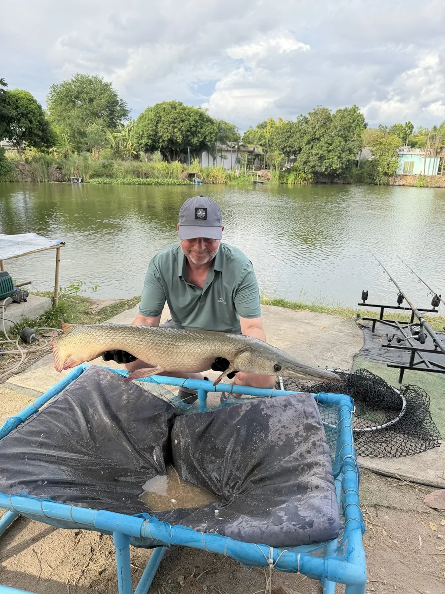 An angler holding a pale fish behind a blue-framed padded cradle at the lake edge