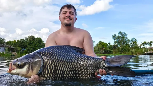 An angler holding a dark scaled fish in the lake at Tight Lines