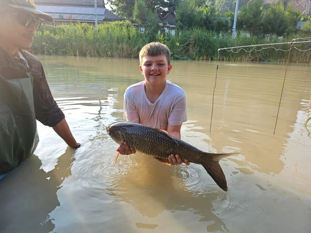 Tyler holding a long scaled fish beside a guide in the lake.