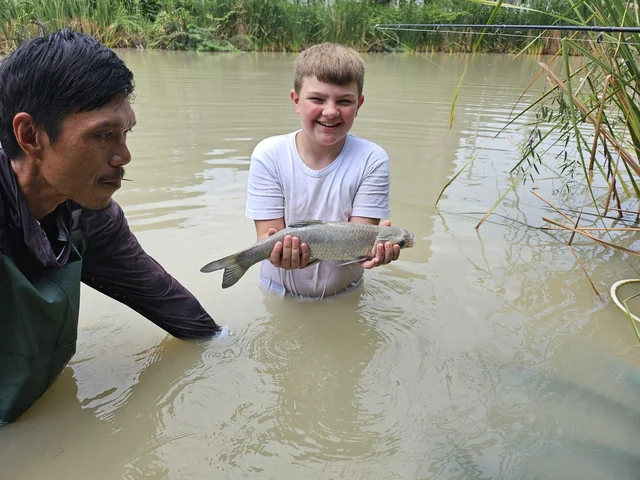 Tyler smiling with a small fish while a guide stands beside him in the lake.