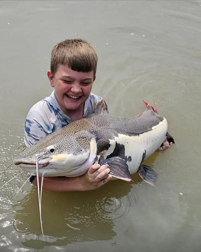 Tyler laughing while supporting a redtail catfish in the lake.